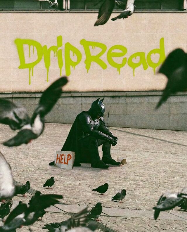 Street-art mural reading &ldquo;DripRead&rdquo; above a figure in a Batman costume sitting on a kerb surrounded by pigeons.